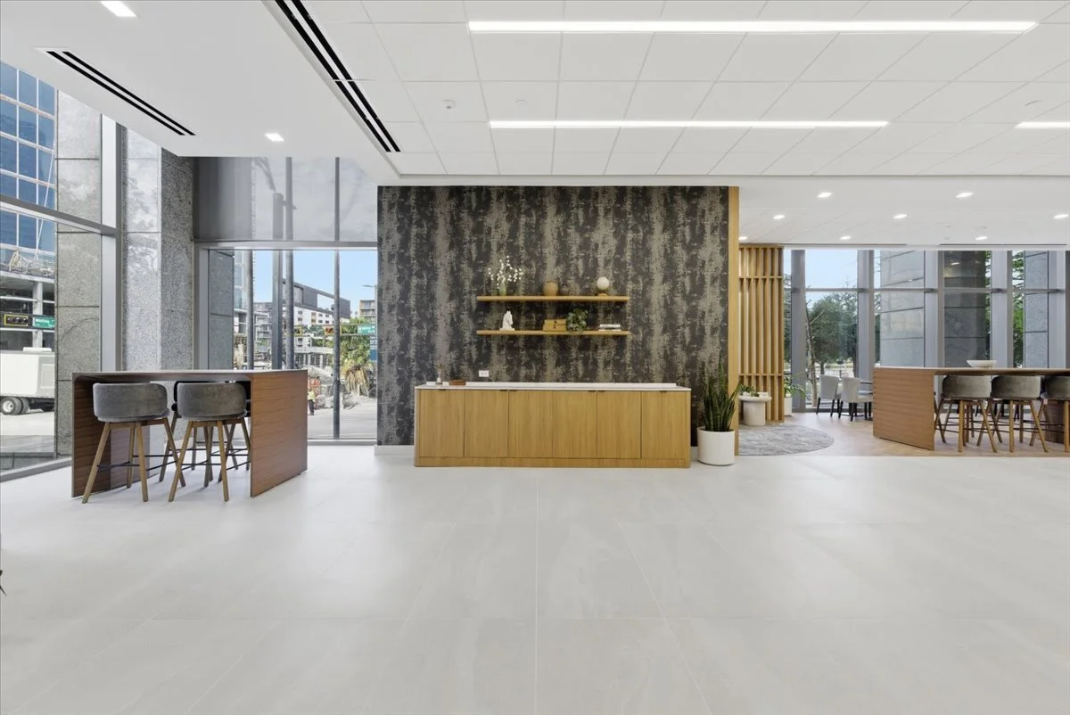 Modern lounge with wooden furniture, decorative shelves, potted plants, and large windows letting in natural light.