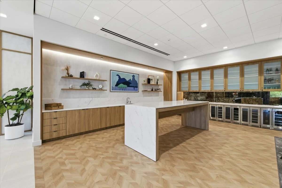 Modern lounge with wooden and marble cabinetry, a large kitchen island, and a built-in wine fridge, decorated with plants and minimalist artwork.