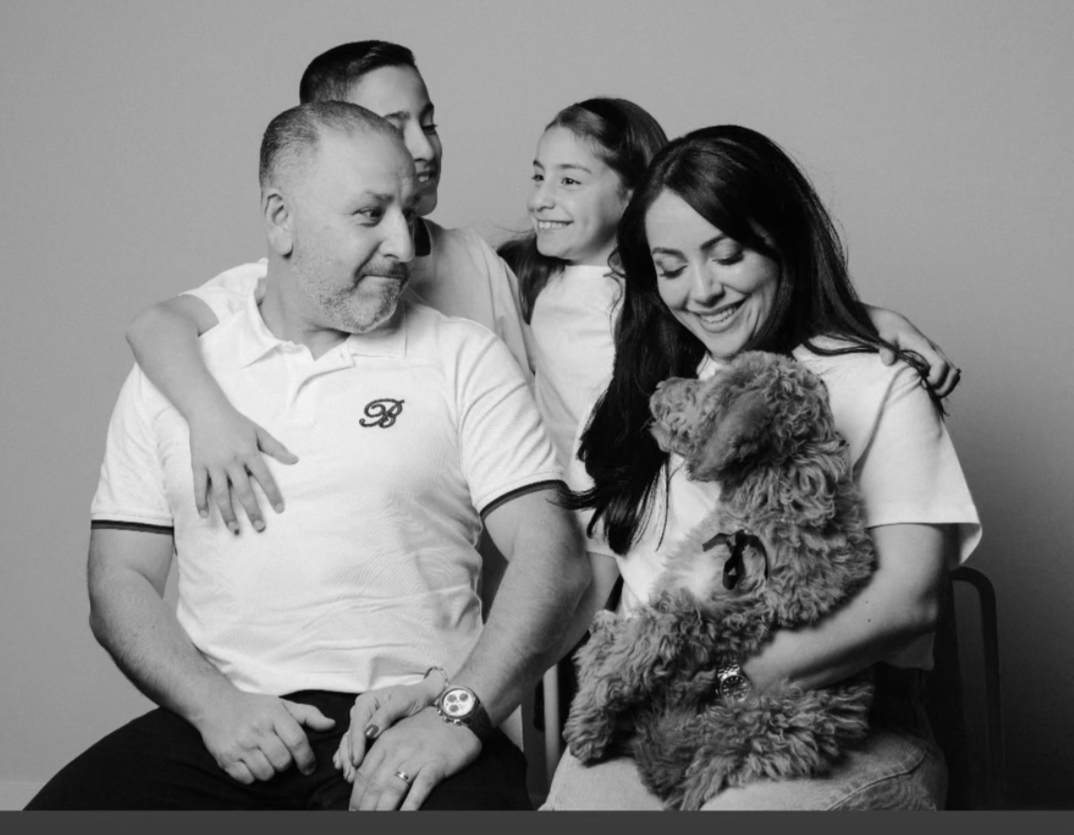 A black and white photo of a family with two adults, two children, and a dog. The woman is holding the dog, and the children are sitting close to the adults, smiling and interacting.