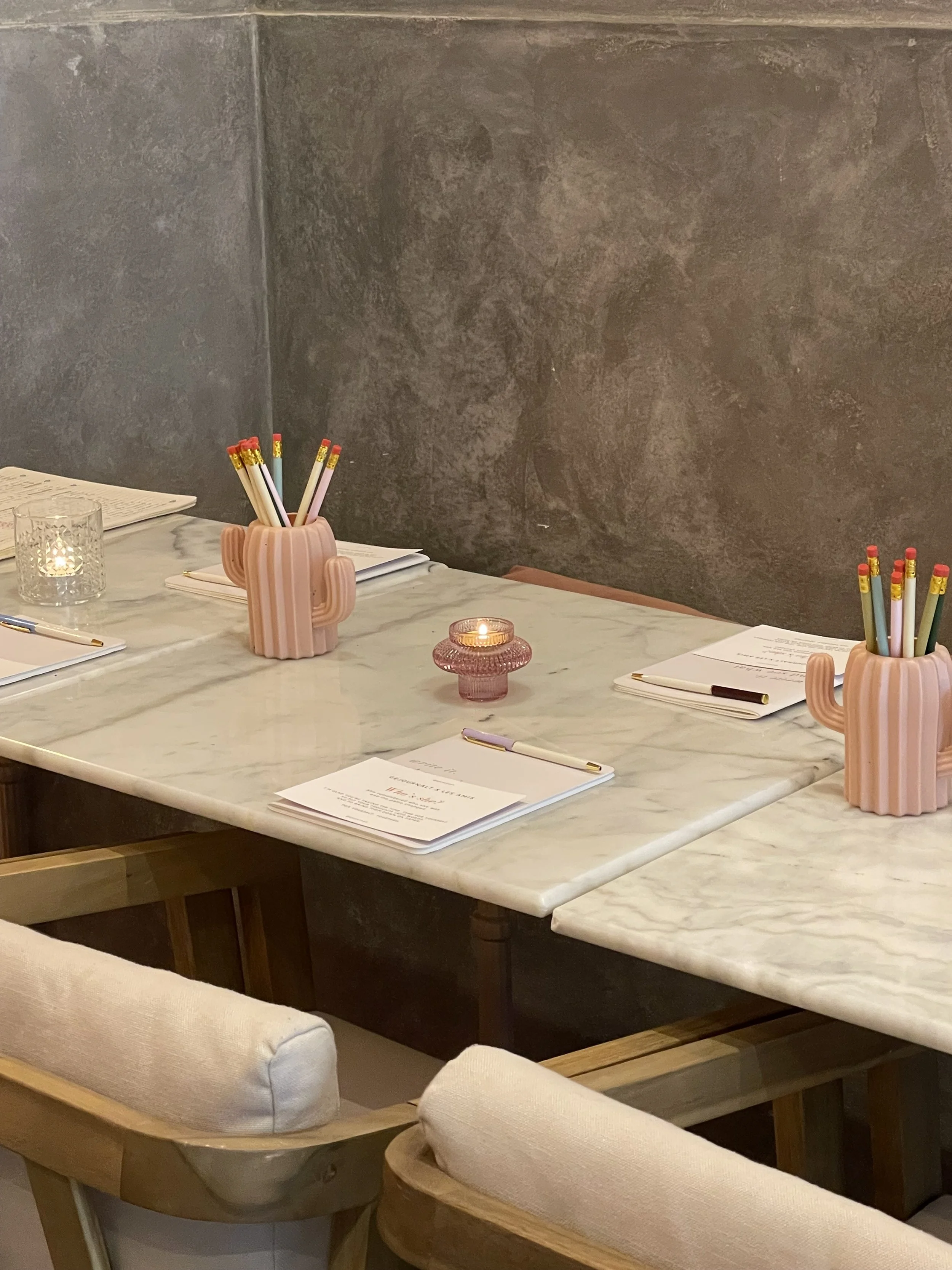 Ein Tisch mit mehreren Stiftgefass, Kerzen, Stiften und Papieren, in einem modernen, gemütlichen Raum.