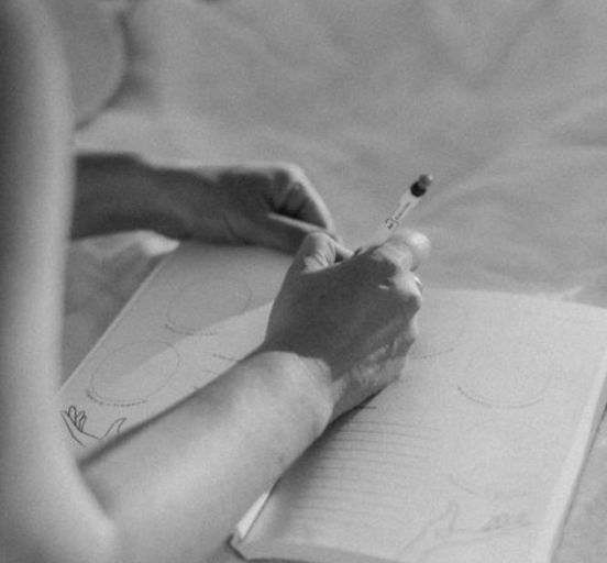 Eine Hand schreibt mit einem Kugelschreiber in einem Notizbuch, das auf einem Tisch liegt, in Schwarz-Weiß