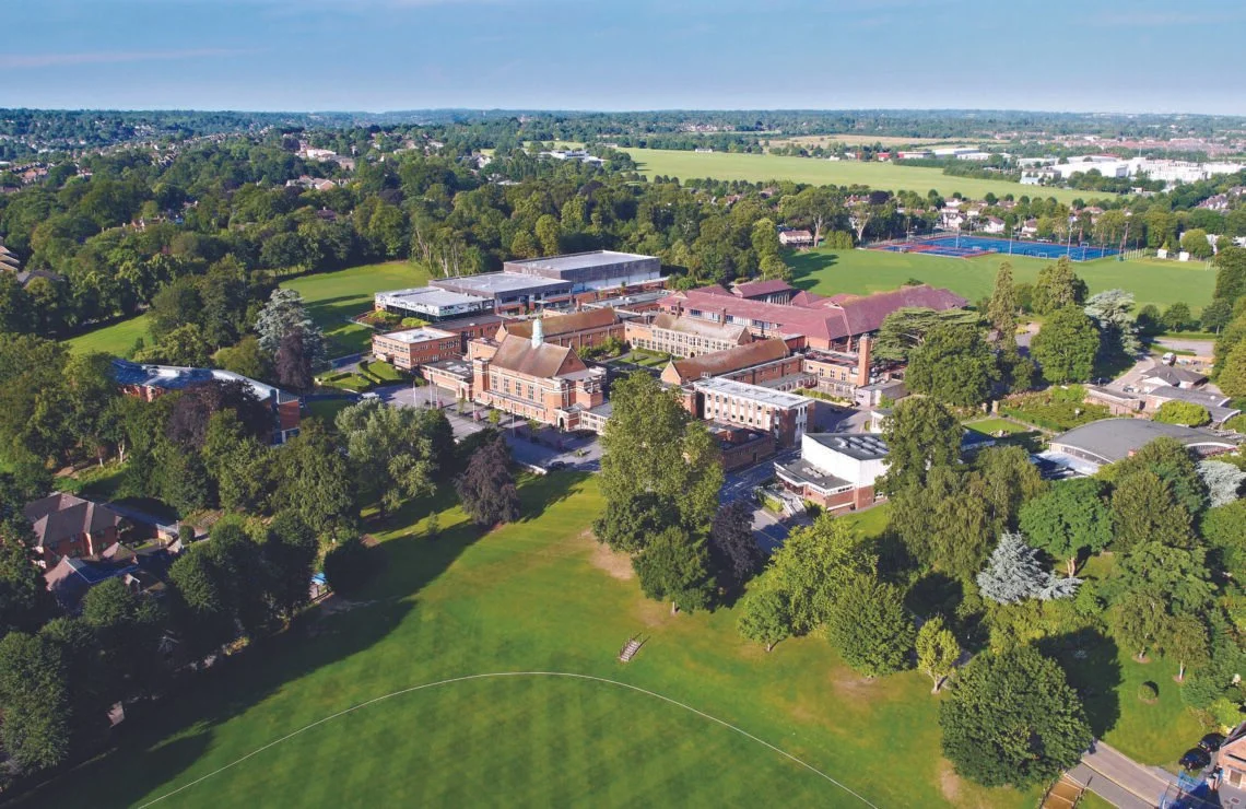 Aerial view of a large private school campus with several buildings surrounded by lush greenery and sports fields.