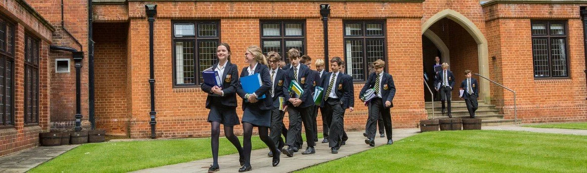Group of co-ed students at boarding school 13+ entry in uniforms walking outside a brick school building.