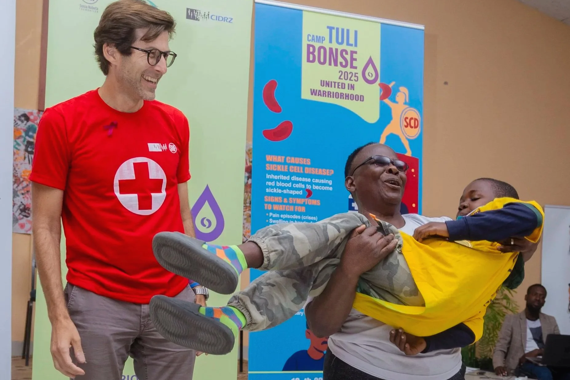  Nurse Pauline Nalungwe, who sees Daniel regularly at the PEN-Plus clinic in Mwachisompola, Zambia, scoops Daniel into the air after he received surprise recognition at the camp’s talent show. Sharing the laughter is Dr. Gene Bukhman, co-chair of the