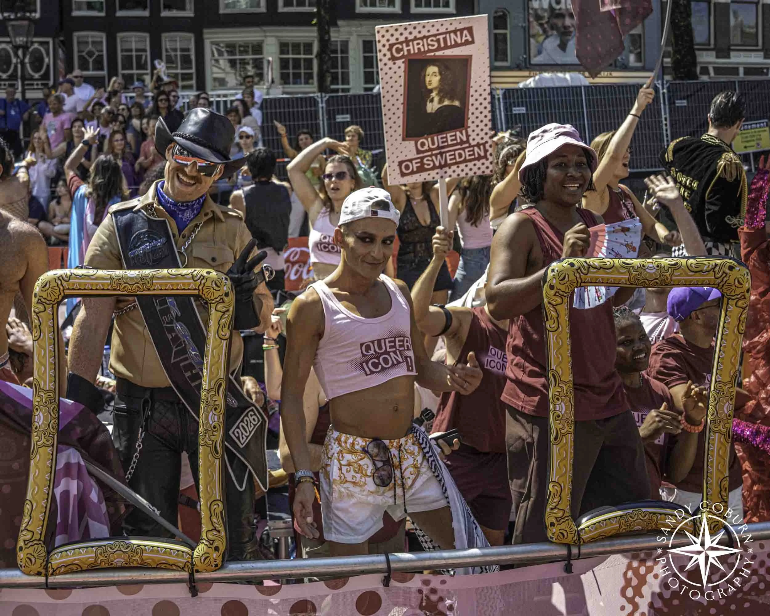 Particpants dance while some hold frames on the Queer Museam boat in at the 2026 WorldPride Amsterdam Canal Parade