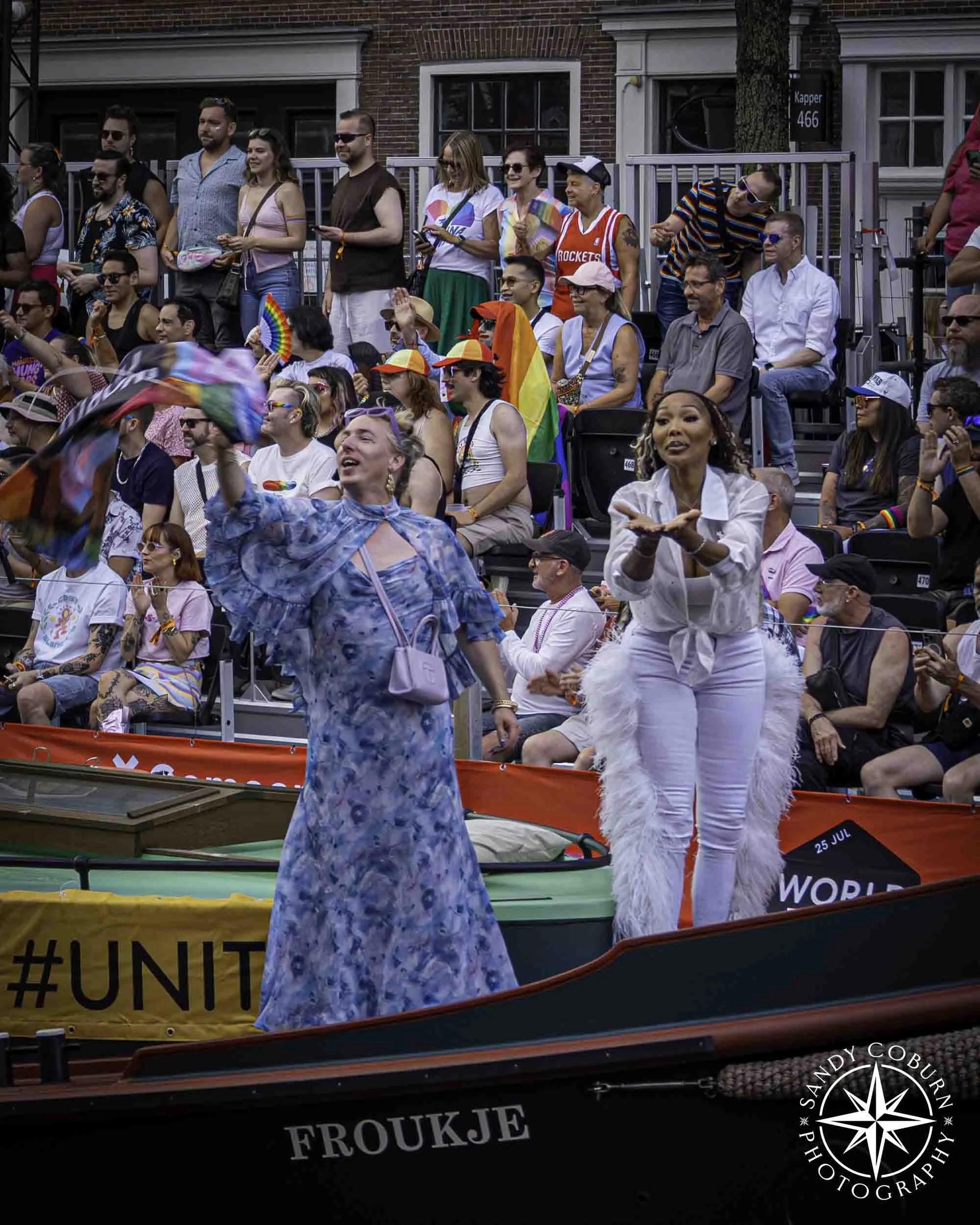 Particpants wave and blow kisses from a boat at the 2026 WorldPride Amsterdam Canal Parade
