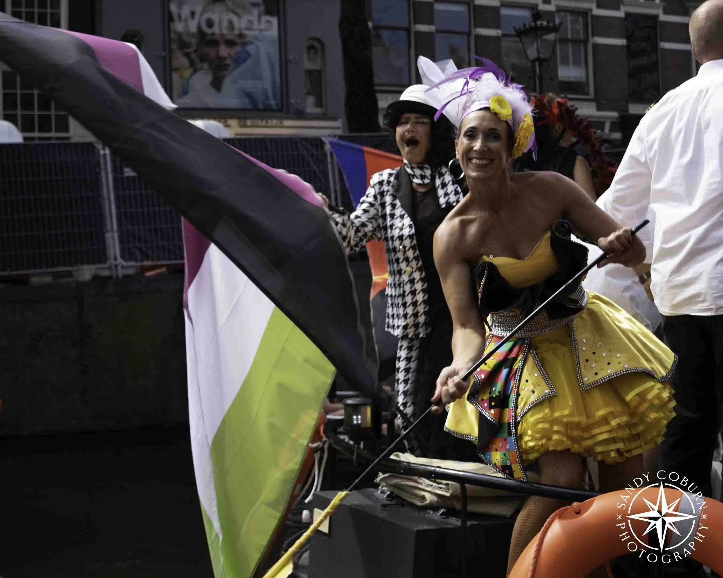 A person in a yellow dress smiles at the photographer from a boat at the 2026 WorldPride Amsterdam Canal Parade