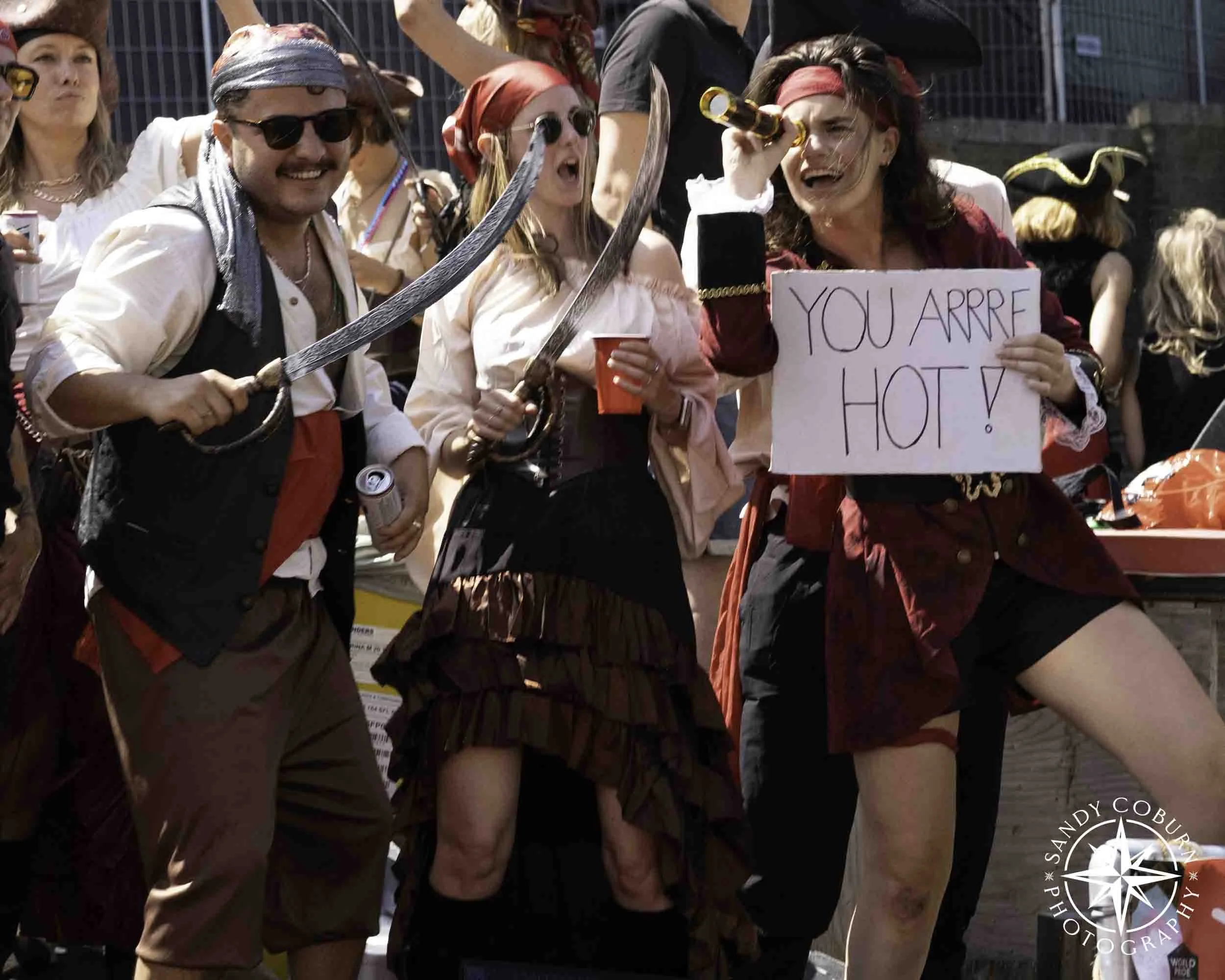 A pirate dons a sign declaring "You arrrr Hot" amid dancers on the YARRR Party boat. YARRR Party is an alternative queer and lesbian collective in Amsterdam at the 2026 WorldPride Amsterdam Canal Parade