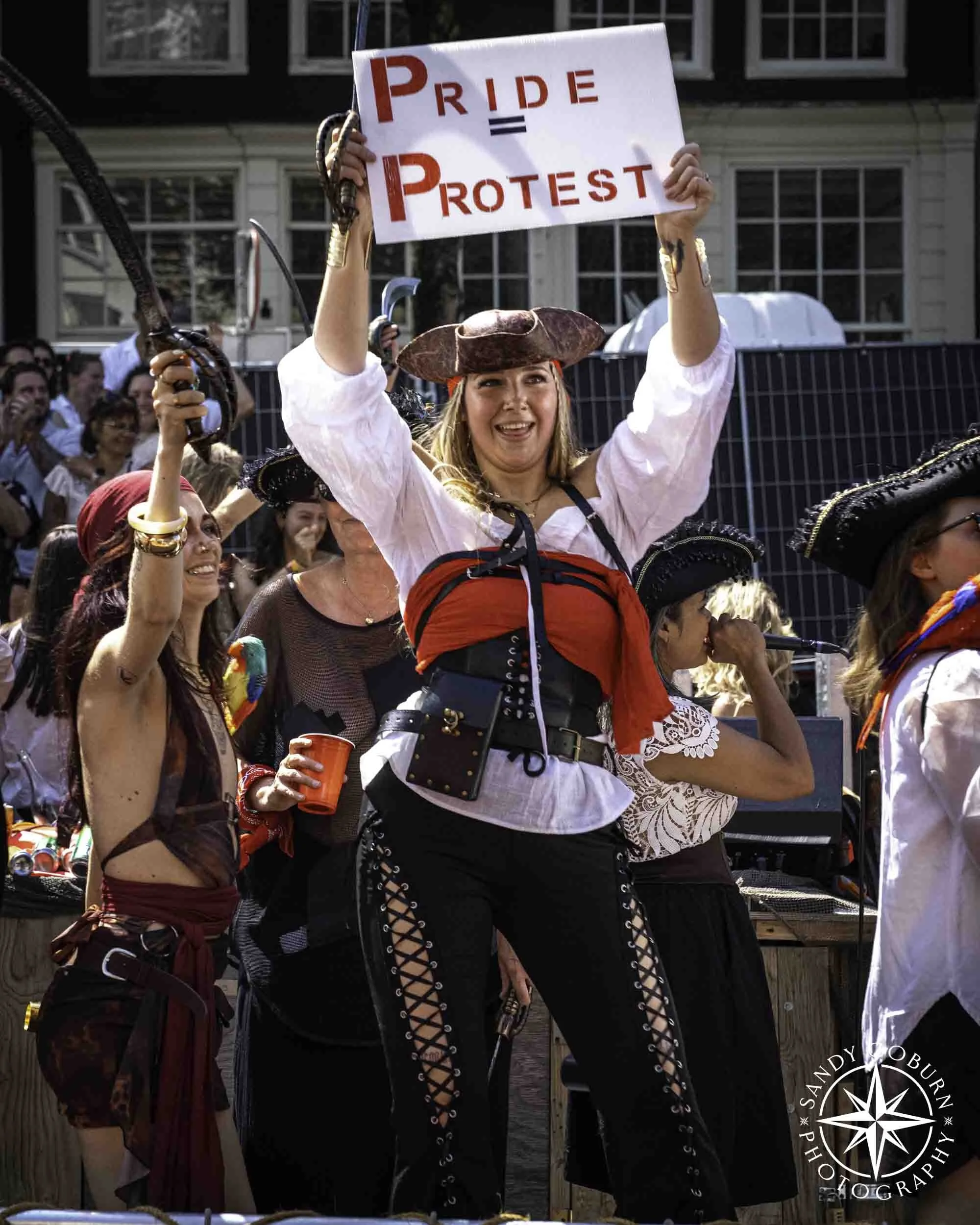 A person dressed as a pirate holds a sign that reads Pride = Protest at the 2026 WorldPride Amsterdam Canal Parade