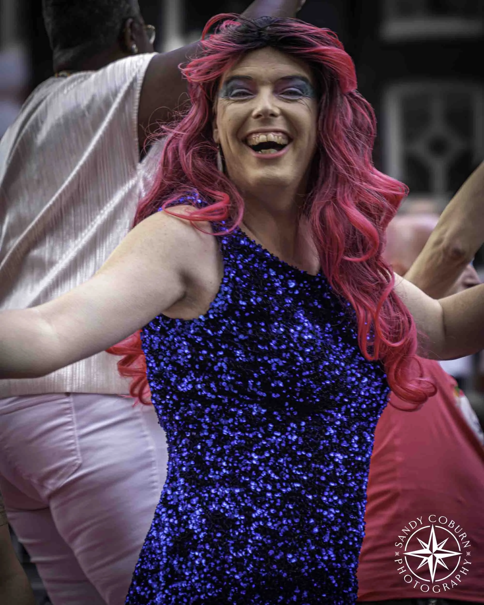 A beaming person with pink hair and a blue dress dances on a boat at the 2026 WorldPride Amsterdam Canal Parade