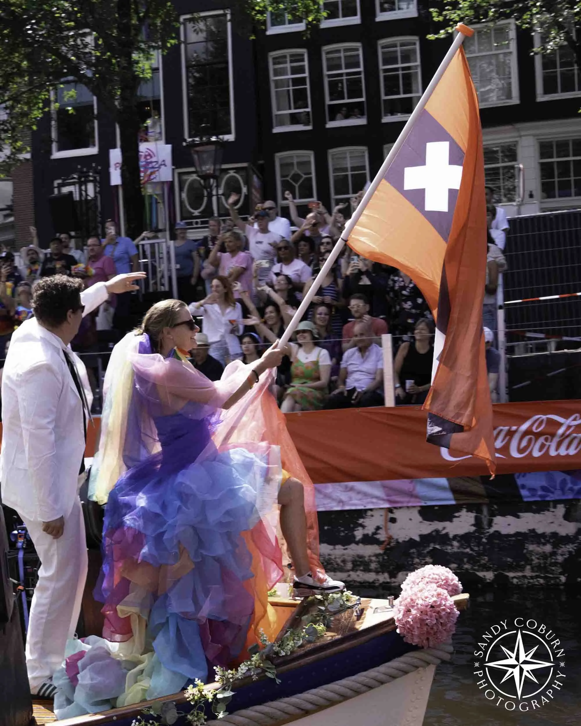 A person waves the Amsterdam flag from a boat at the 2026 WorldPride Amsterdam Canal Parade