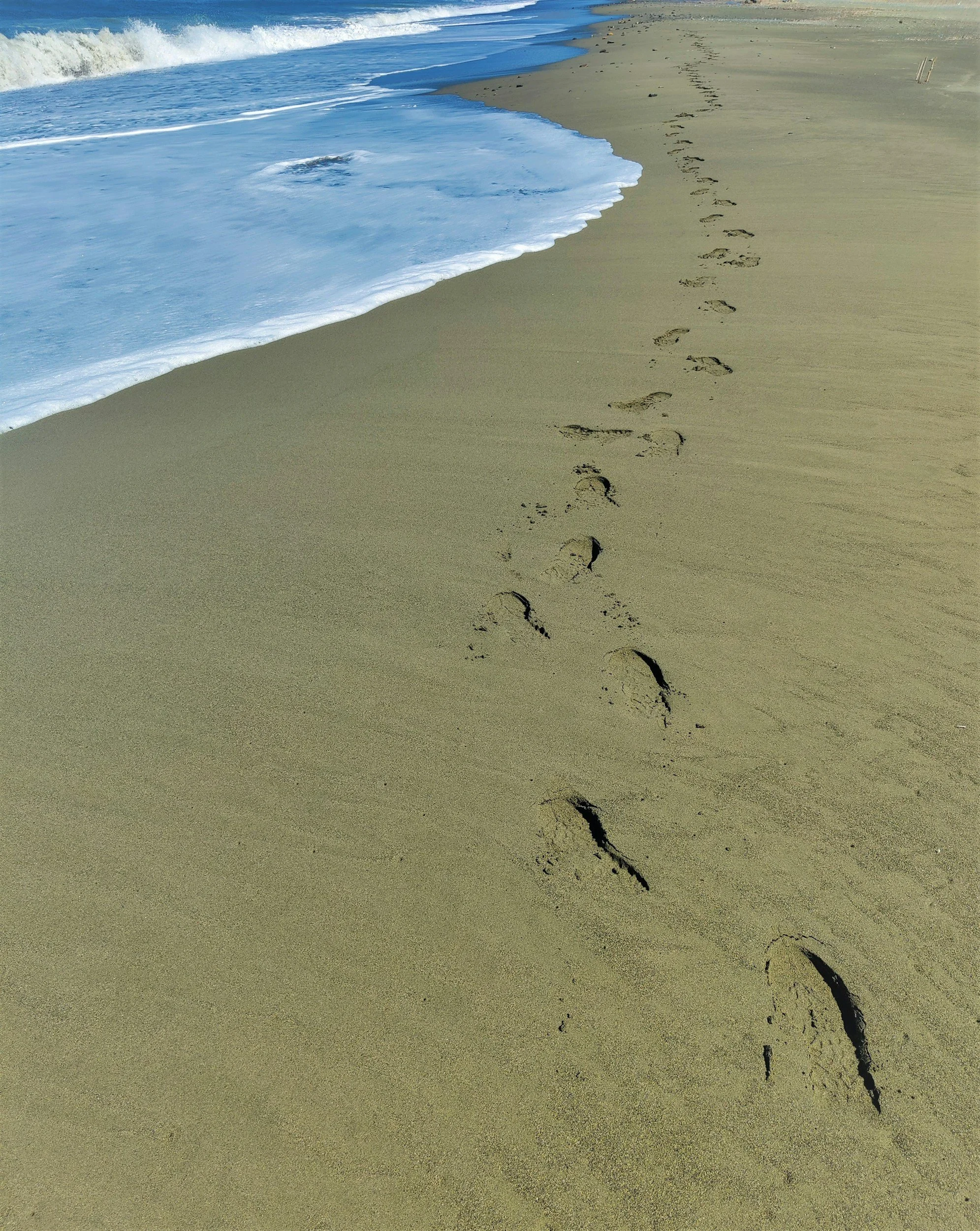 Footprints in the sand on a beach leading towards the water and waves.