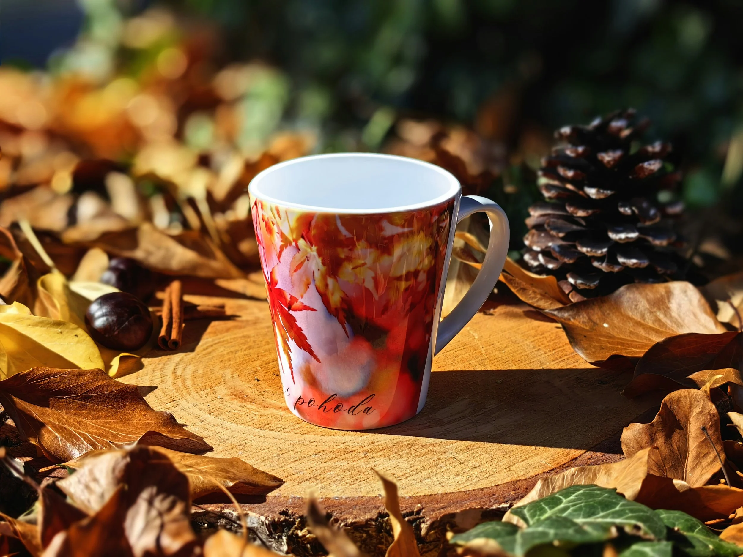 Decorative mug with fall foliage design on a tree stump surrounded by autumn leaves, pine cone, and acorns.