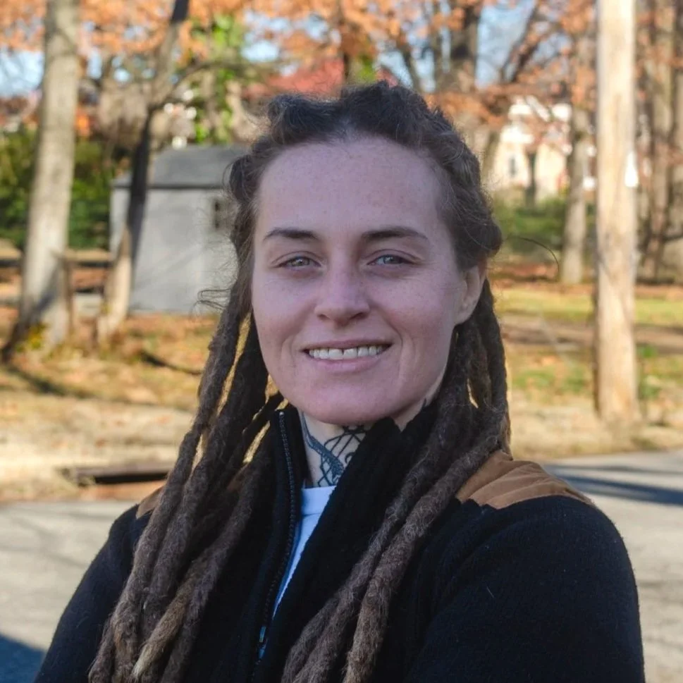 Woman with dreadlocks smiling outside at night in an urban area.