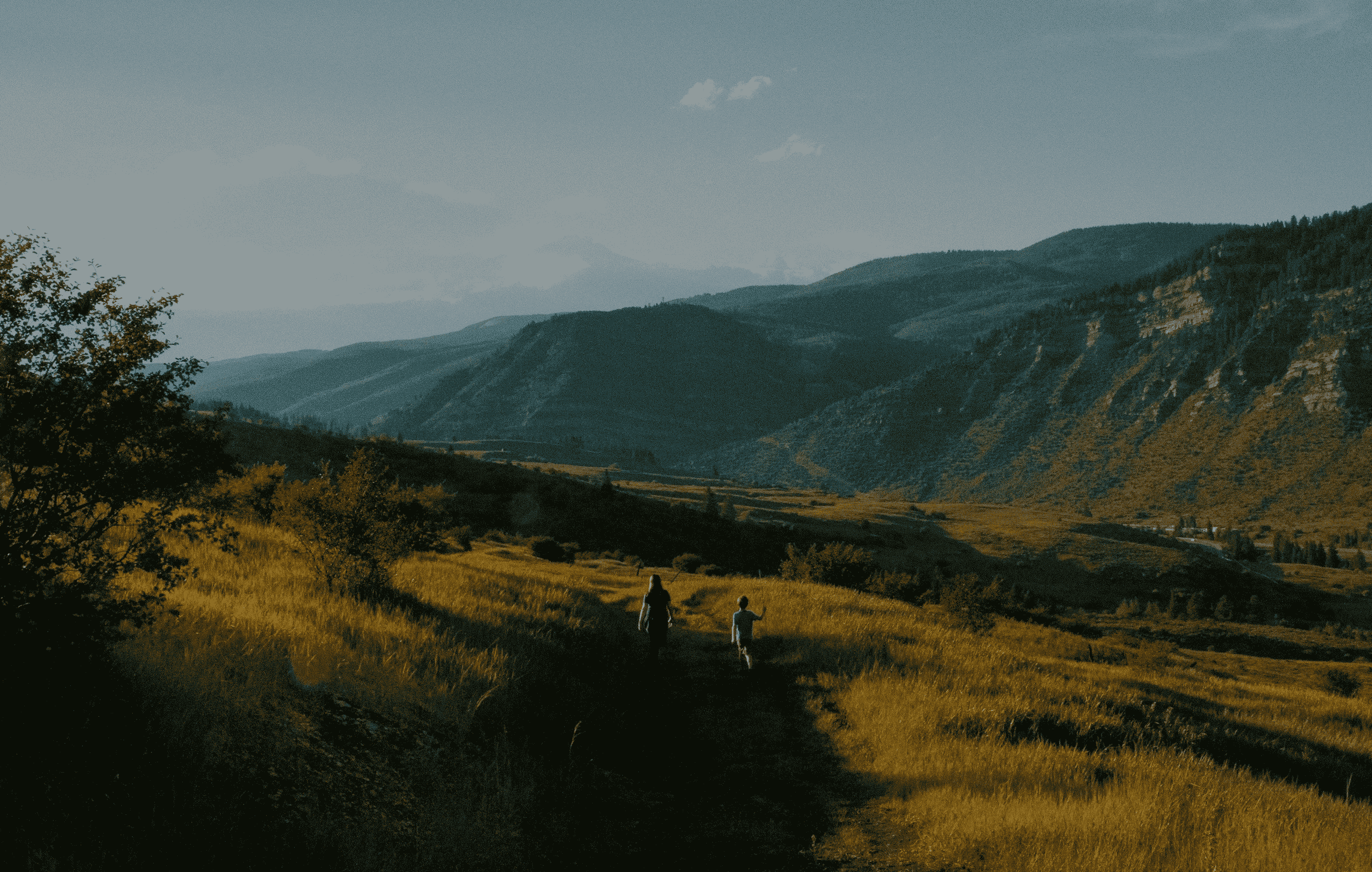 Two people walking on a path with green hills in the background