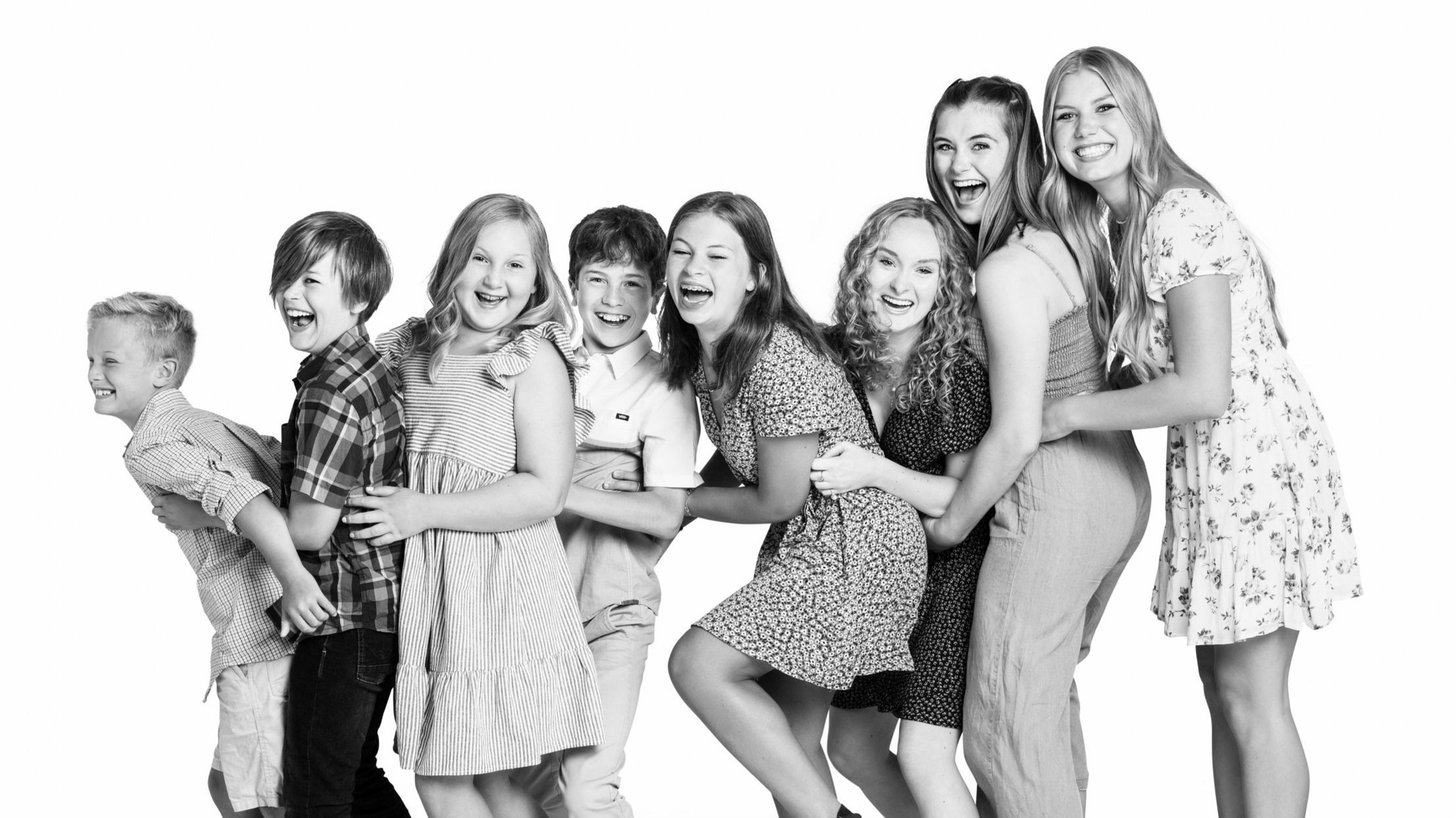 Fun black and white kids studio portrait of siblings and cousins lined up hugging each other, taken by a Seattle children's photographer.
