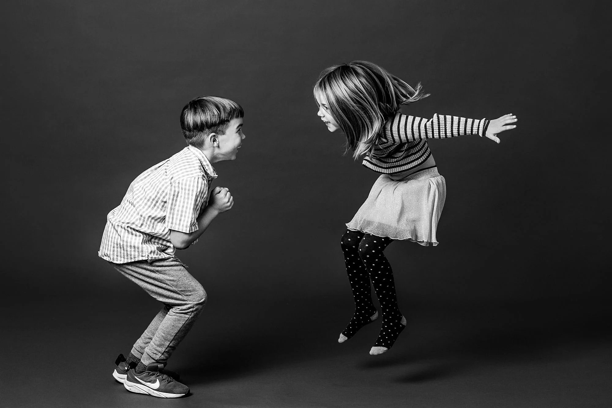 Playful black and white action portrait of a brother and sister jumping together in studio, taken by a Seattle kids photo studio.