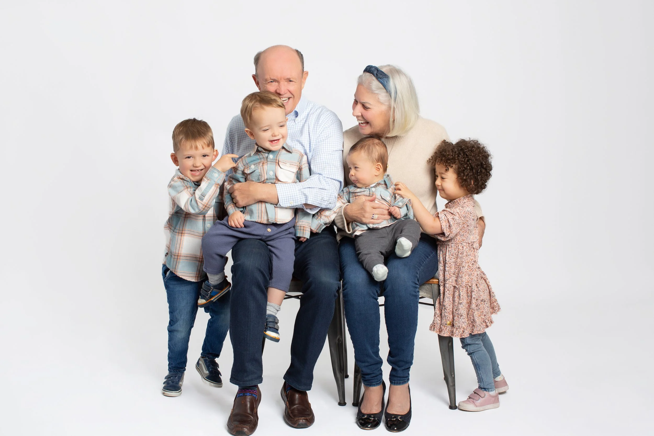 Studio family portrait of grandparents sitting with their four young grandchildren on a seamless white background, captured by Smallish, a Seattle family photographer.