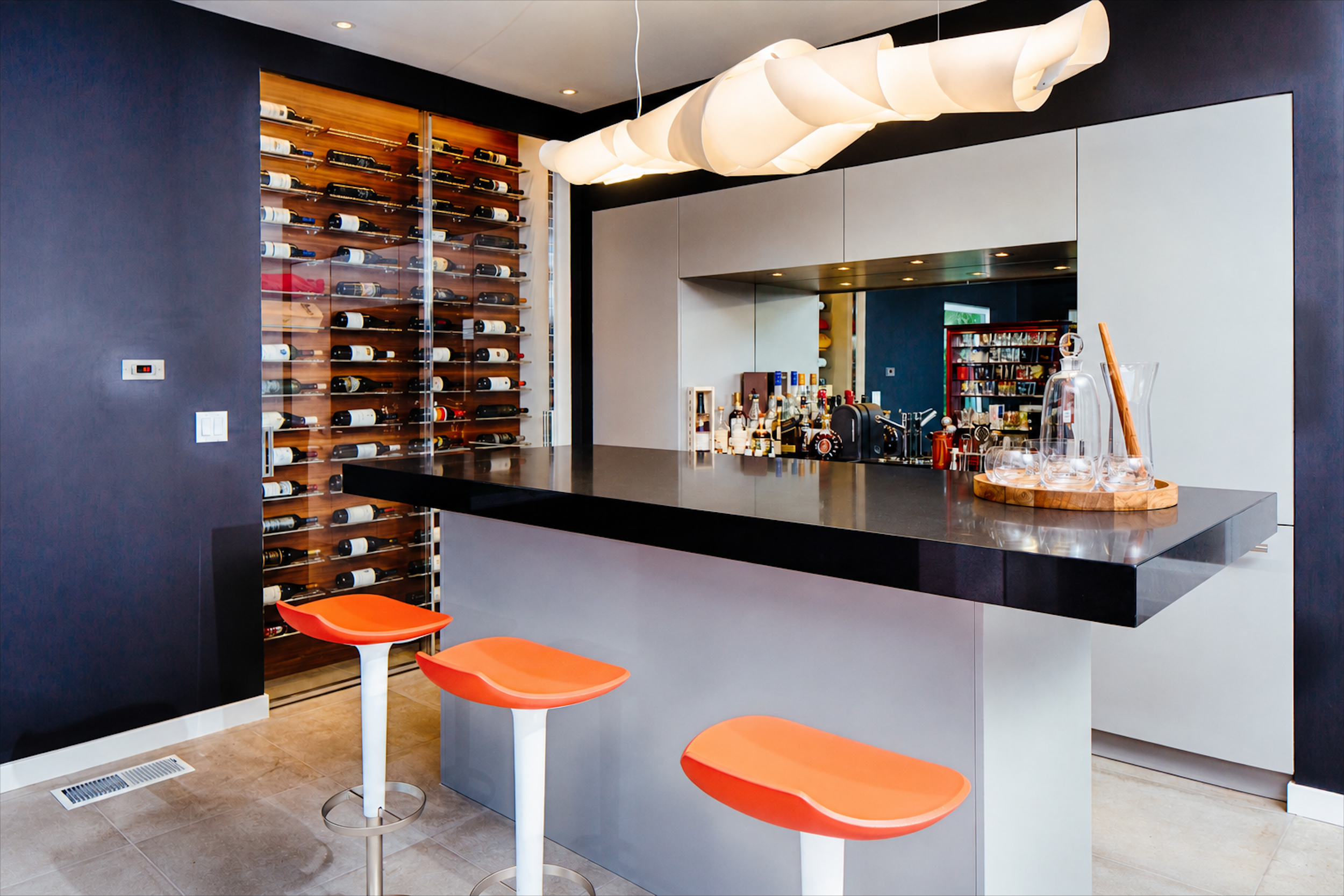 Entertainment bar with black countertop, orange stools, and floor-to-ceiling wine storage