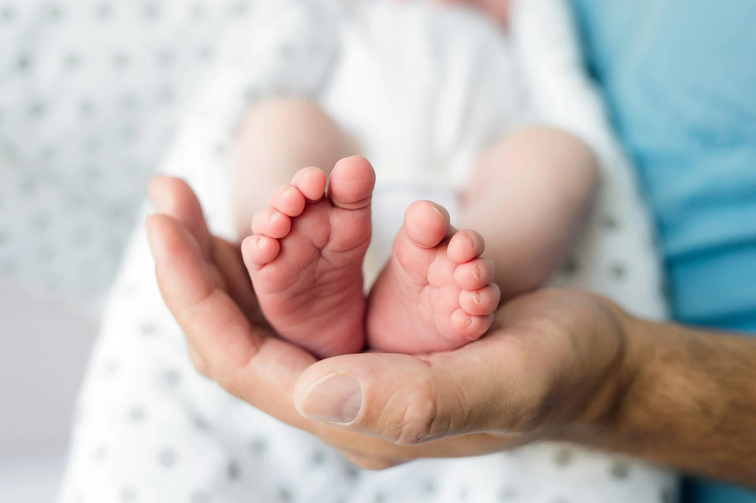Close-up of an adult hand gently holding a tiny baby's foot.