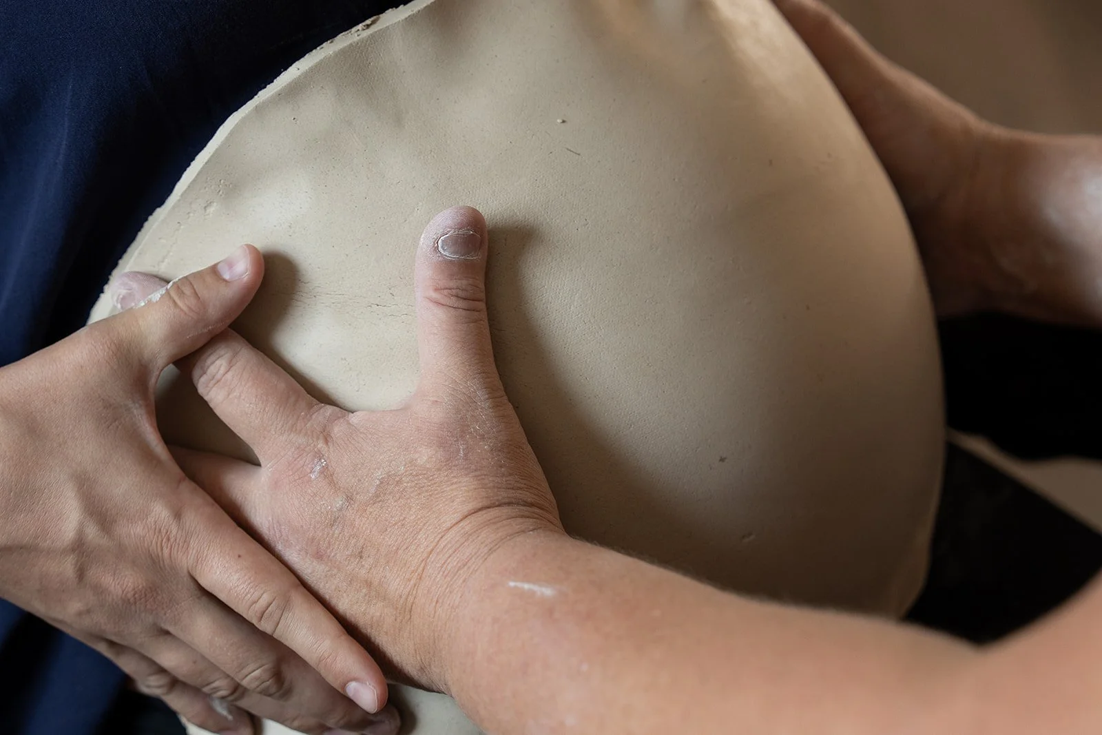 Close-up of a person shaping clay on a pregnant belly with their hands, focusing on their thumb and fingers pressing into the clay.