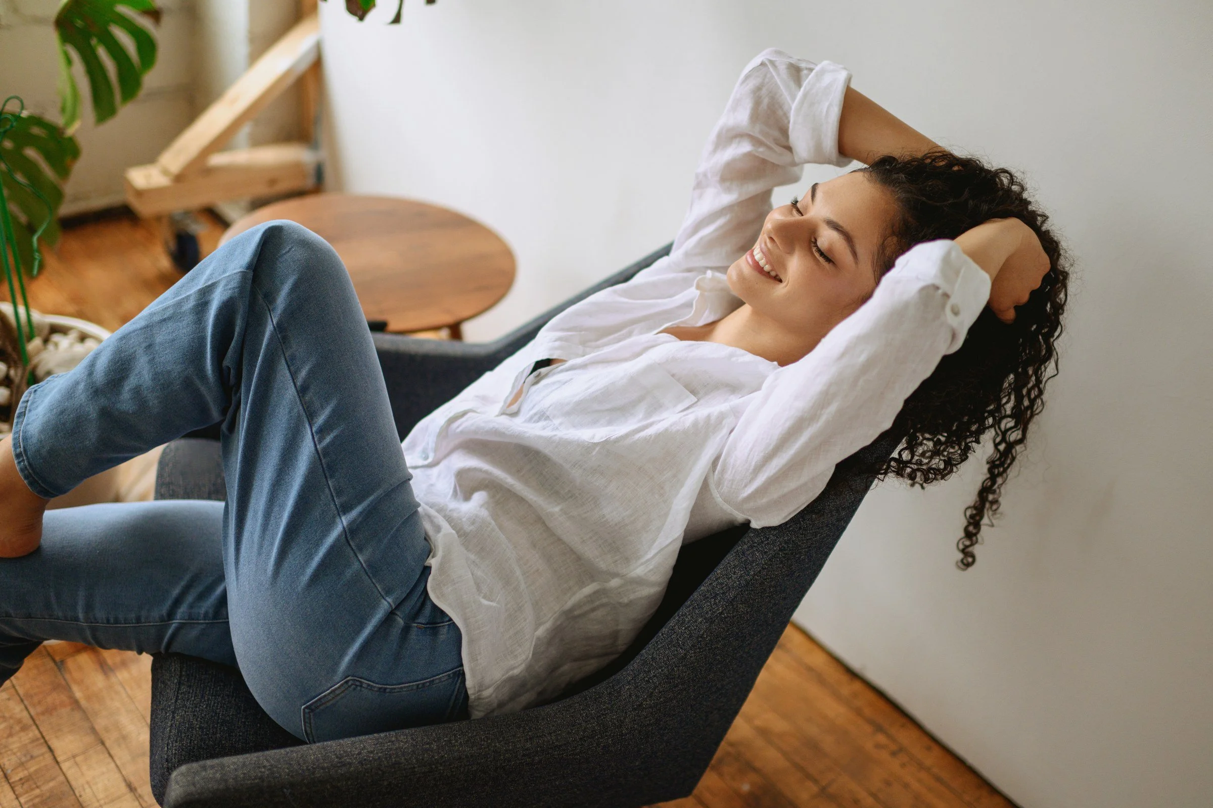 Karol reclining in a blue chair, wearing a white shirt and jeans at Location A Studios.