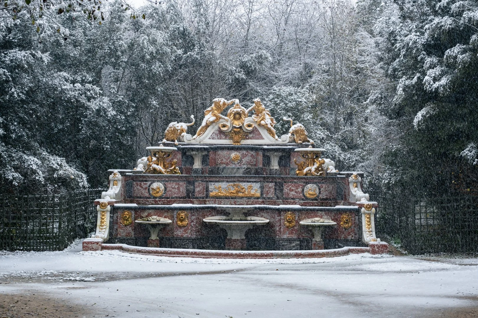 A decorative fountain covered in snow, surrounded by trees with snow on their branches.