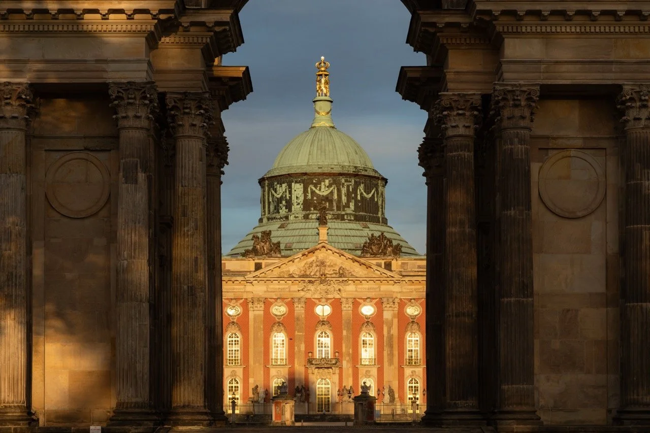 View of an ornate building with a large dome, framed by grand stone columns in the foreground, during sunset.