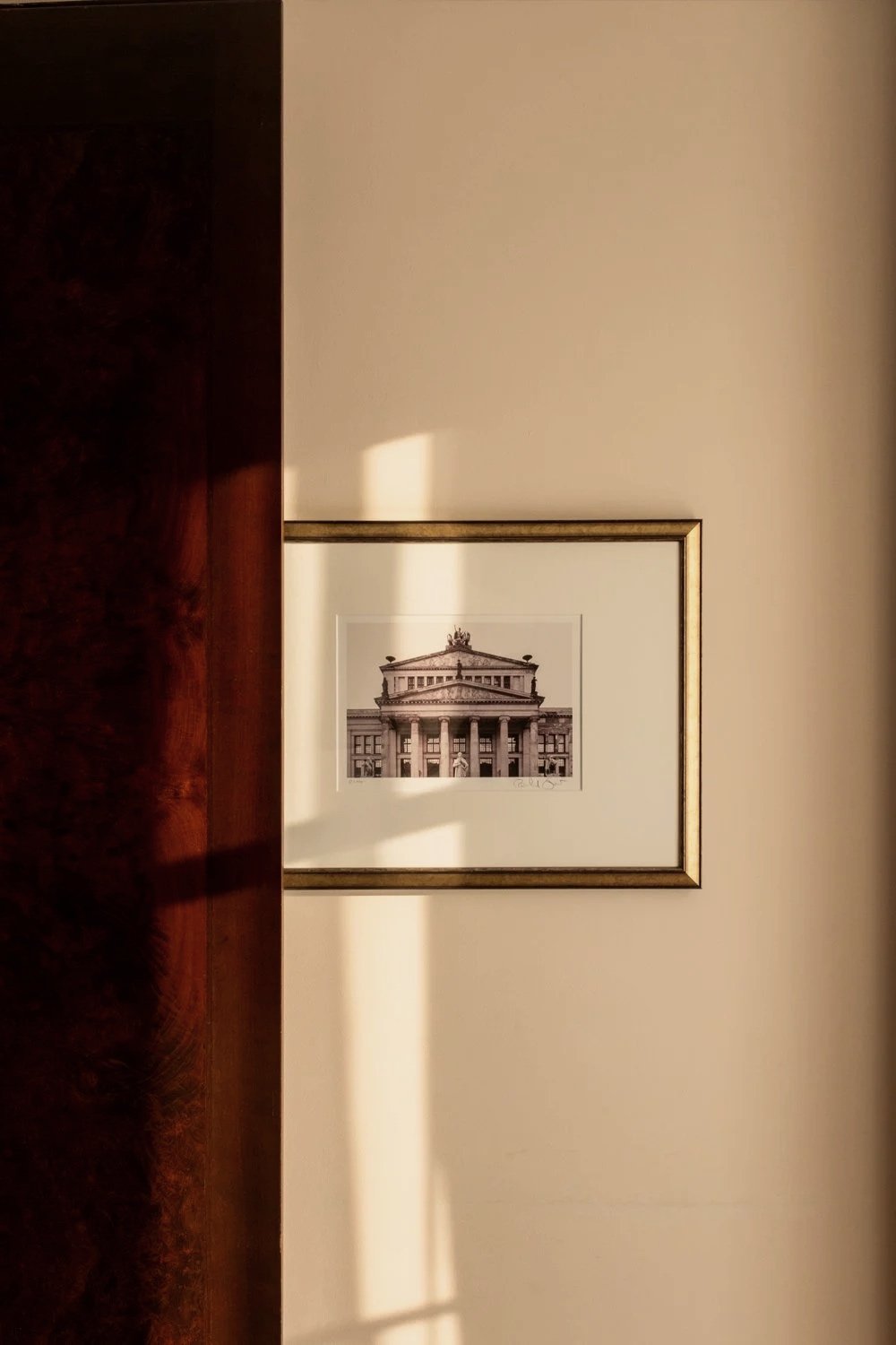 Close-up of a framed black-and-white photograph of a classical building on a beige wall, partially obscured by a dark wooden door.