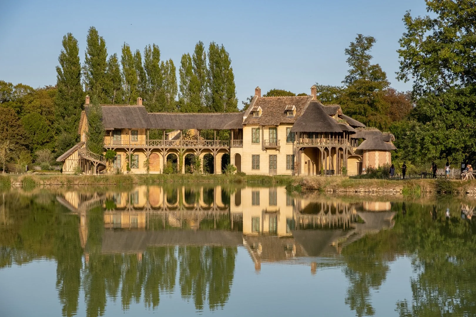 Historic house by a lake, surrounded by trees, with a reflected image in the water.