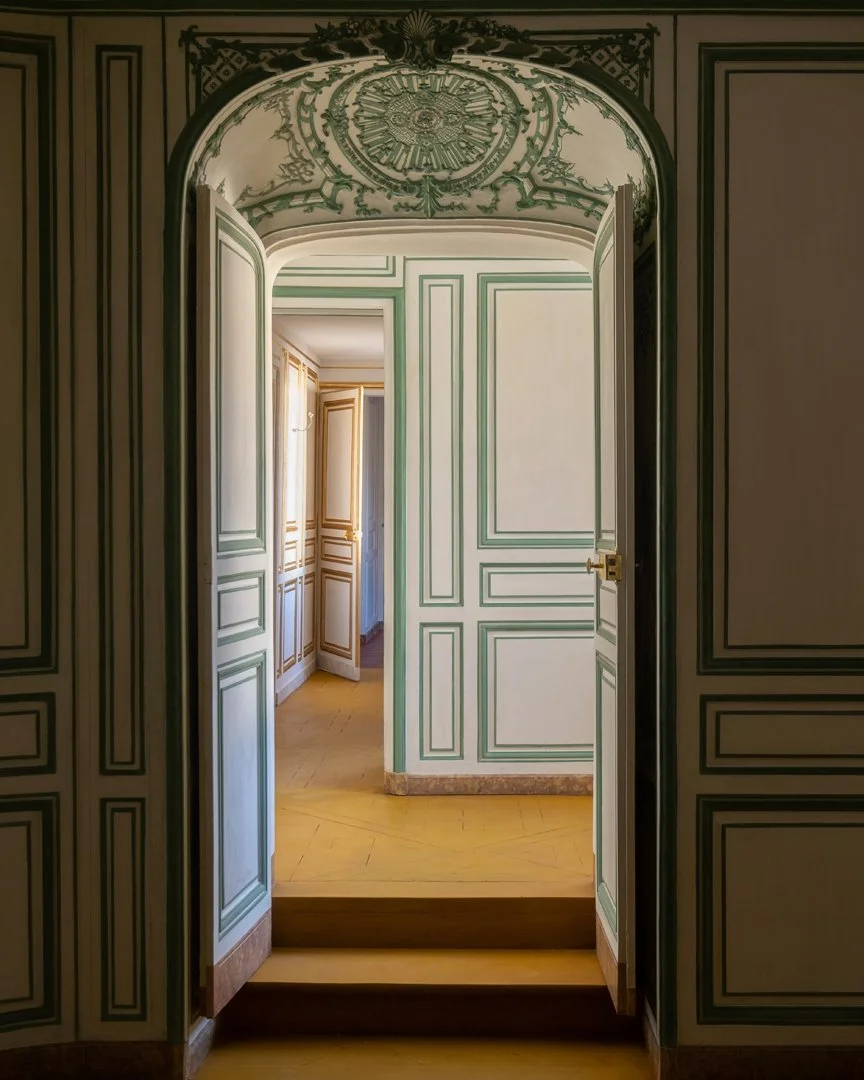 View through an ornate doorway into a room with intricate wall paneling and a wooden floor.