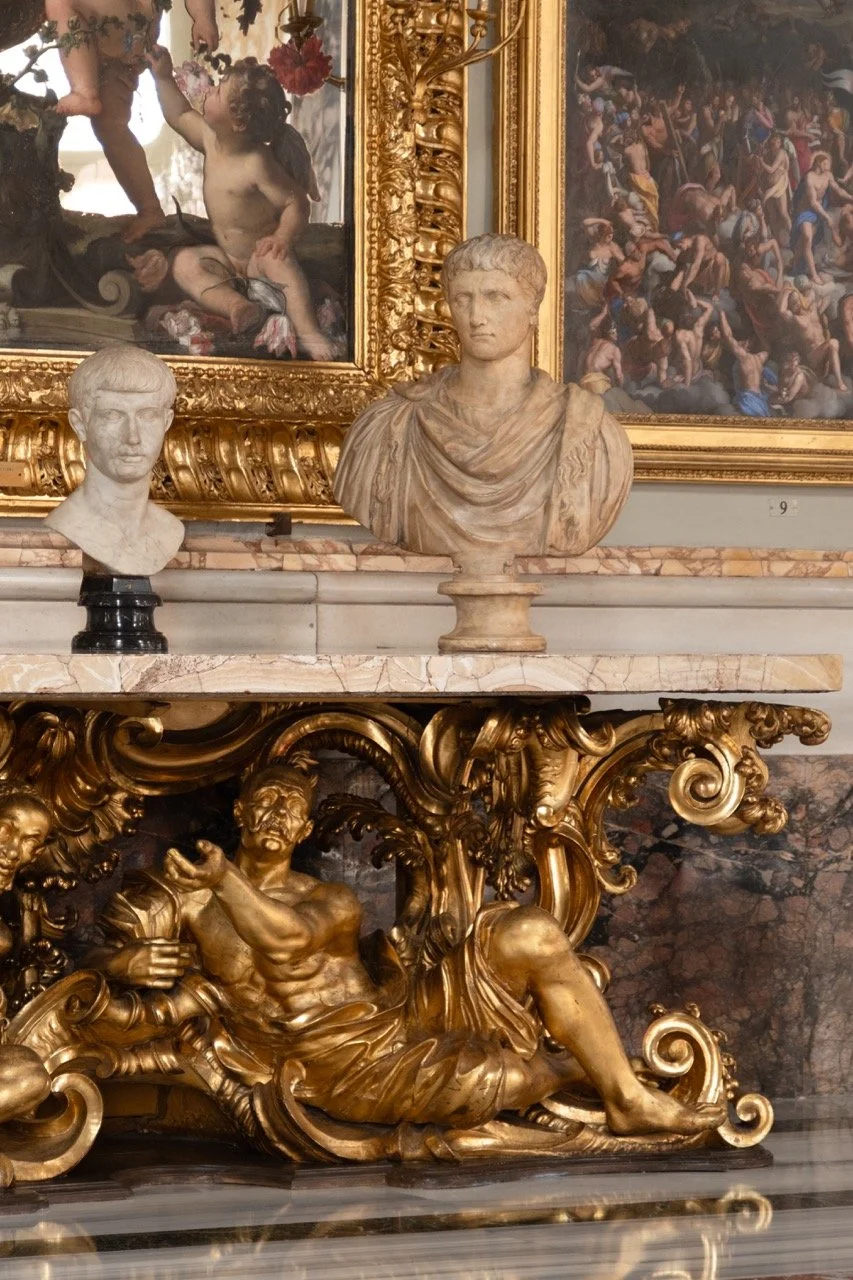Classical marble busts and sculptures on ornate gold and marble surfaces, with paintings in the background featuring historical and mythological scenes.