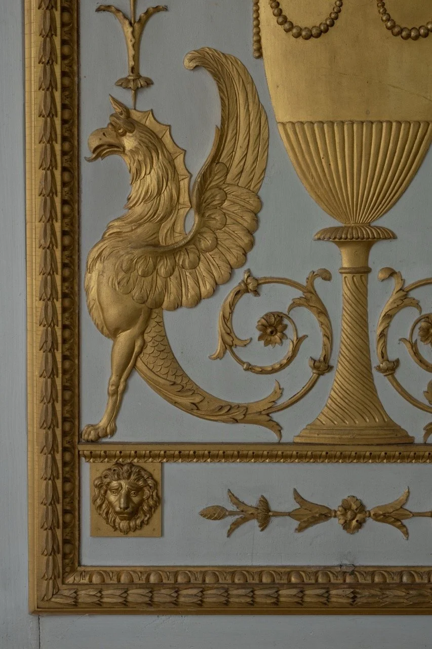 Ornate wall panel featuring a golden griffin, a golden vase, and decorative floral and lion head elements.
