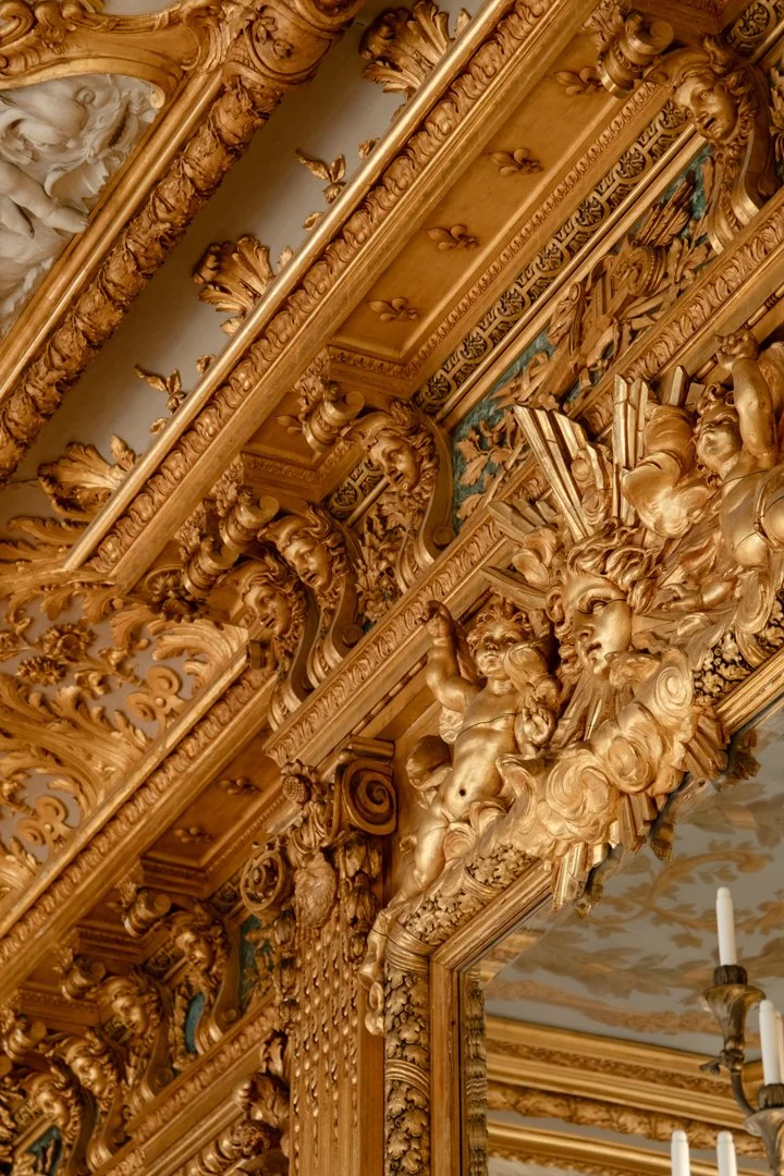 Ornate gold gilded ceiling with intricate carvings of cherubs, faces, and floral motifs, featuring detailed sculptures and decorative architectural elements.