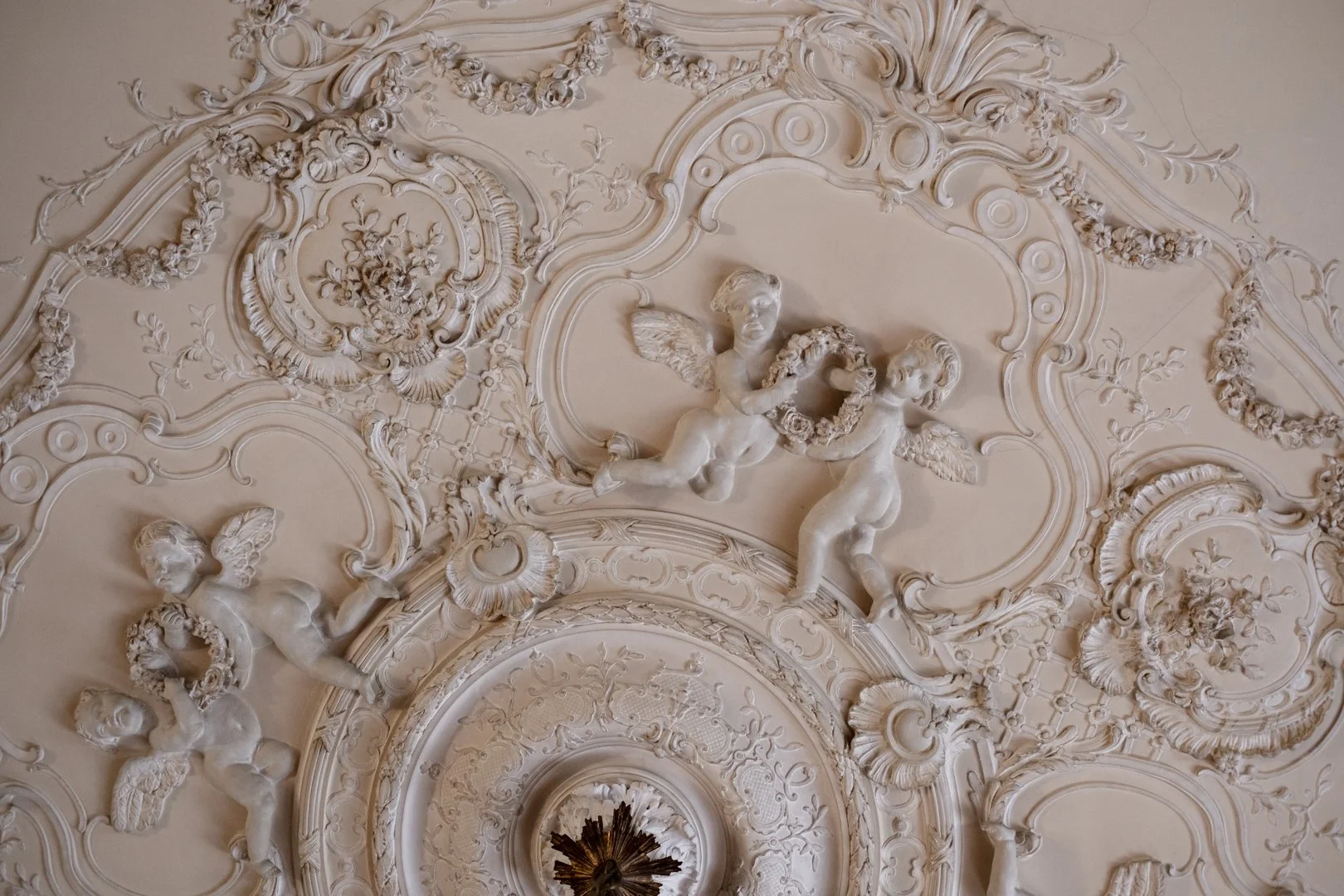 Ornate ceiling with decorative plasterwork and cherubic sculptures with wings.