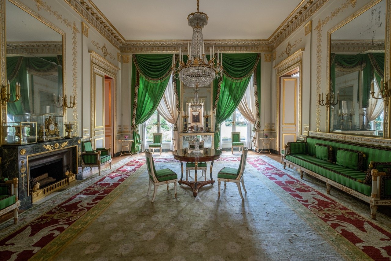 Elegant room with green curtains, a chandelier, and vintage furniture including chairs, a sofa, and a mirror.