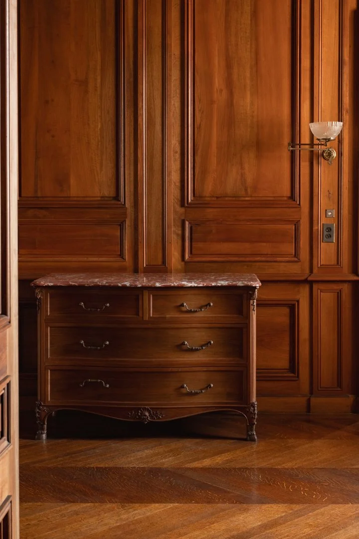 A wooden dresser with a marble top in a room with wooden panel walls and hardwood floors.