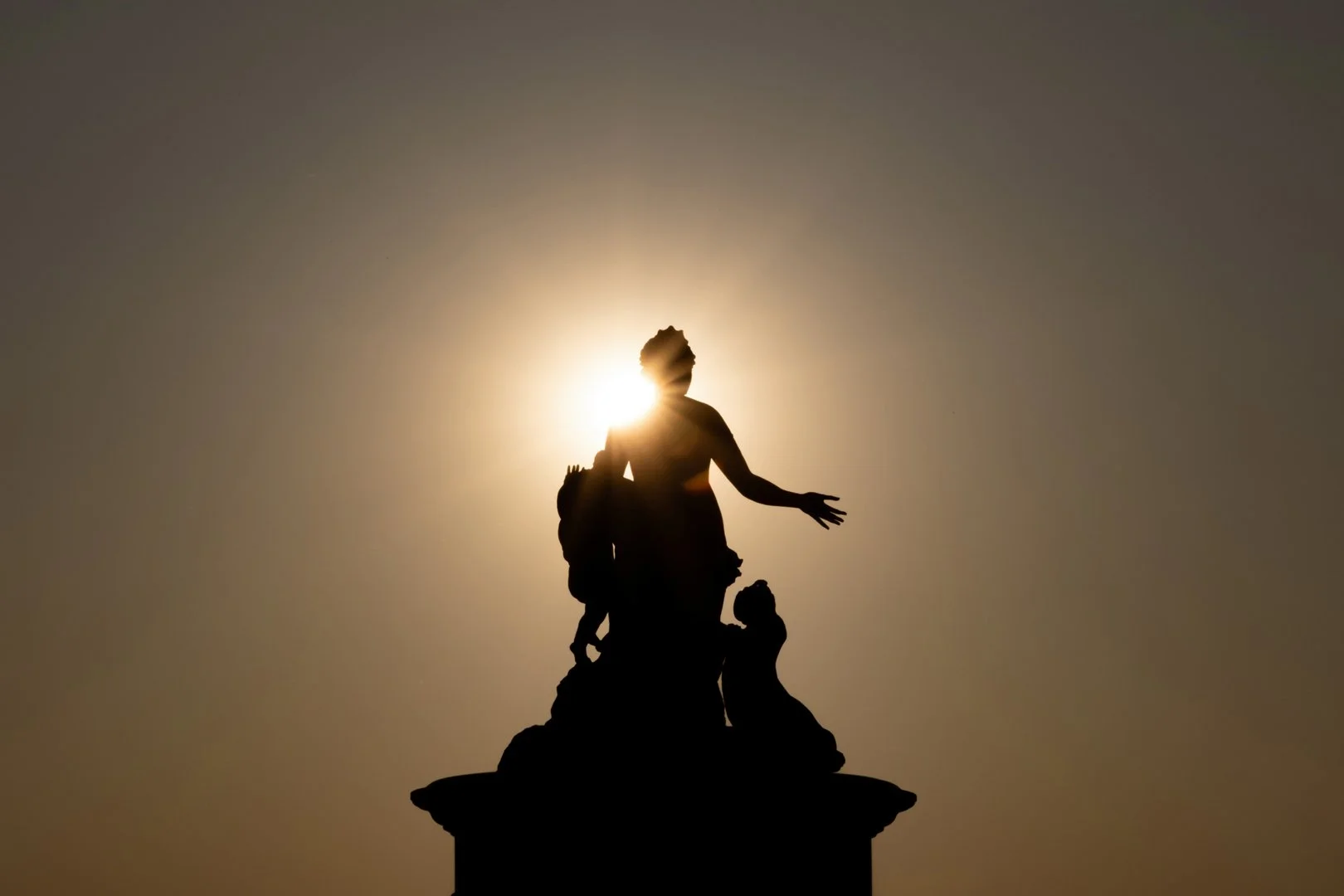 Silhouette of a woman with children at sunset, with the sun behind her creating a halo effect.