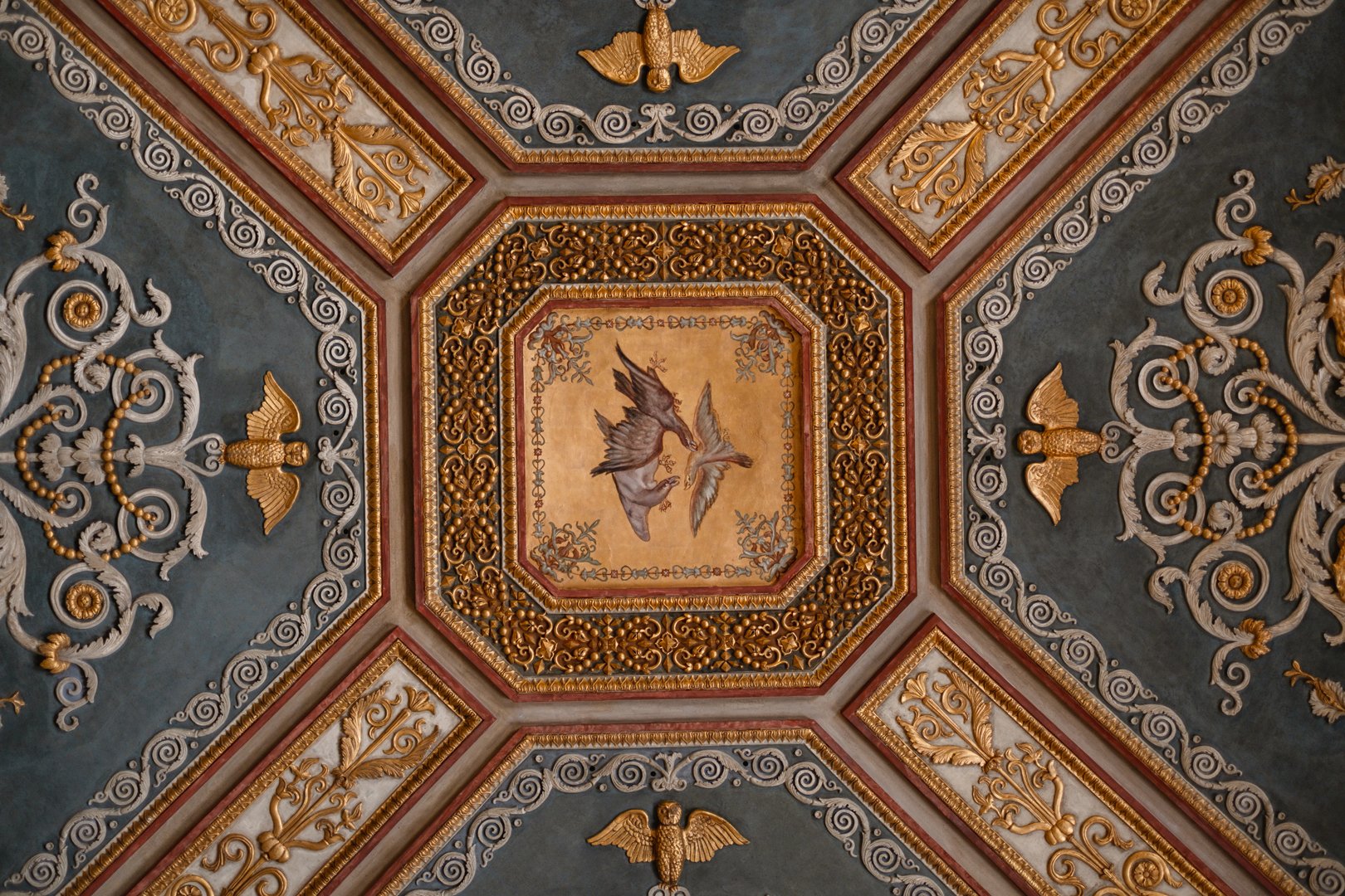 Ceiling with ornate gold and tan decorative molding, featuring motifs of birds, angels, and intricate scrollwork.