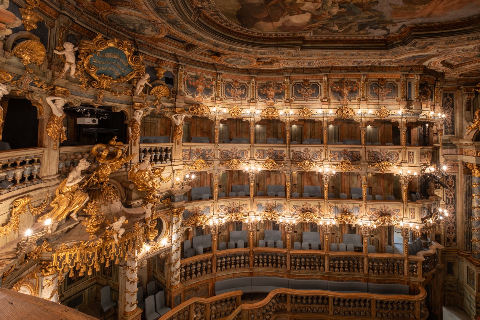 Interior of an ornate theater with gold decoration, statues, and multiple balconies with seating, decorated with intricate patterns and lighting.