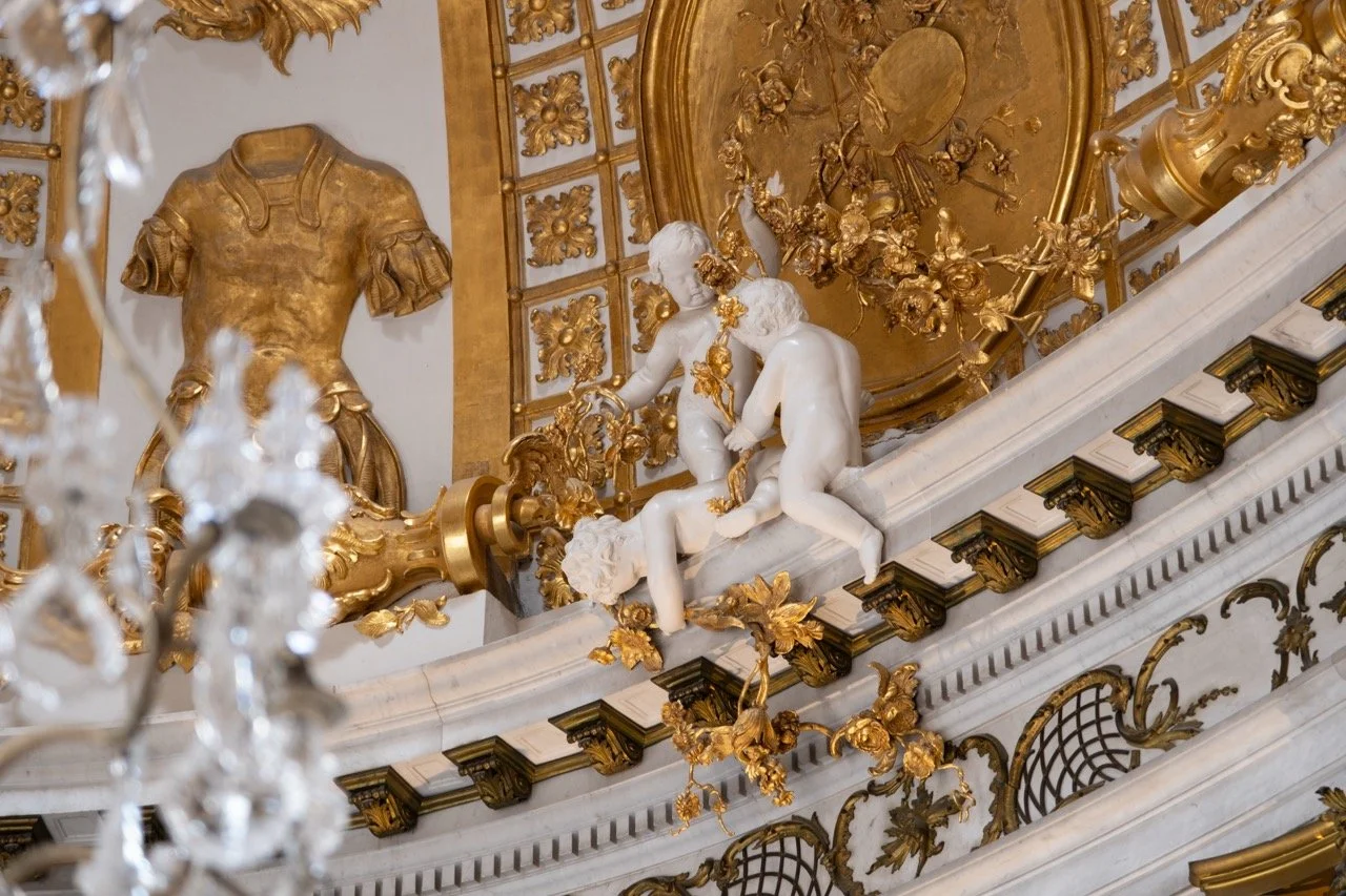 Ornate ceiling with gold accents, sculptures of children, and decorative wall features.