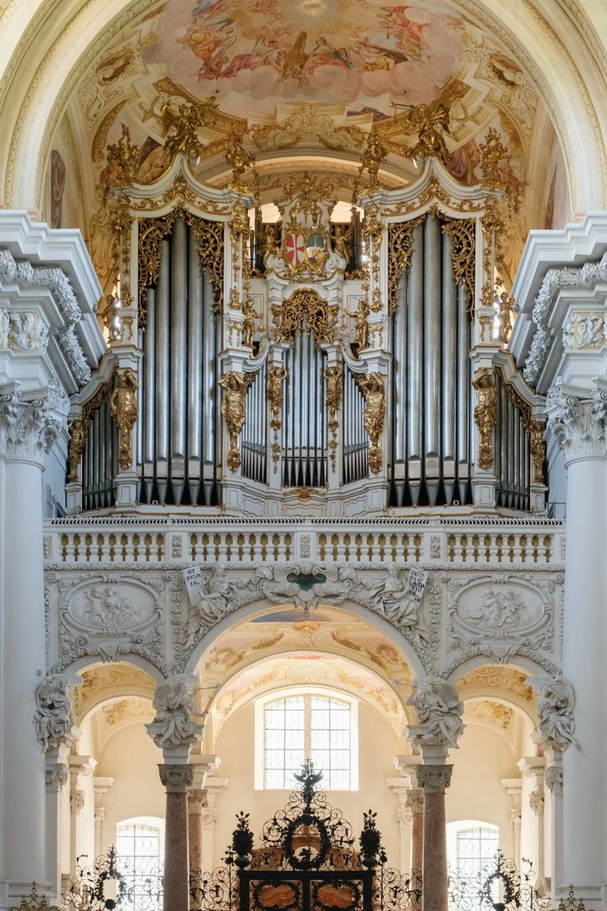 Baroque-style church interior with elaborate gold and white decorations, large pipe organ, and ornate columns and carvings.