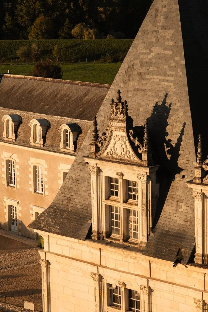 Close-up of an ornate rooftop atop a historic building, with detailed stone carvings and tall, narrow windows, illuminated by golden sunlight.