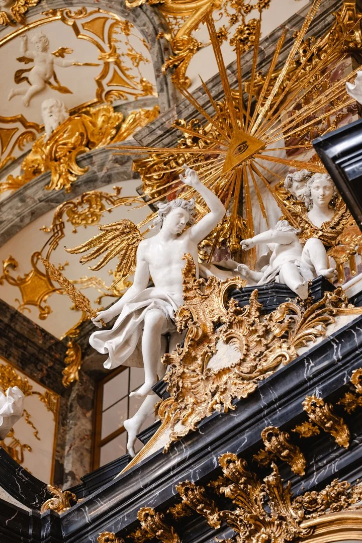 Baroque-style sculpture with white marble angel and cherubs surrounded by gold gilded ornamental details and dark marble accents.