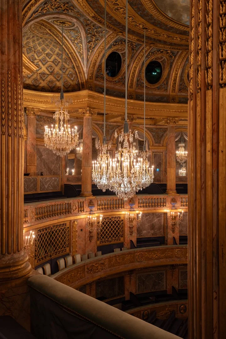 View of an ornate theater balcony with chandeliers and gold detailing.