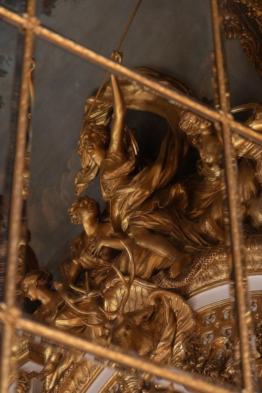 Gold ornate sculptures of mythical creatures and figures, including a woman holding a spear, displayed behind a decorative iron grille.