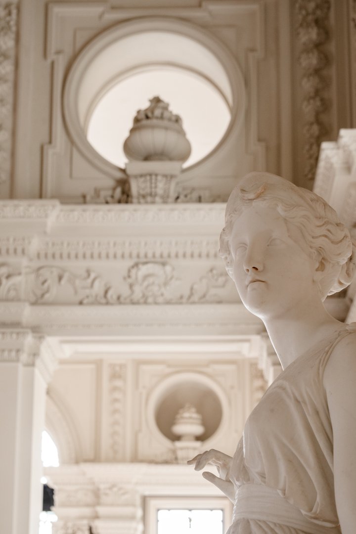 Marble statue of a woman in an ornate indoor setting with high ceilings and decorative architectural details.