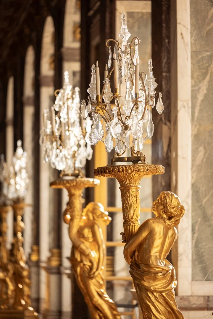 Elegant gold statue holding a crystal chandelier, with similar chandeliers and ornate decor in the background.