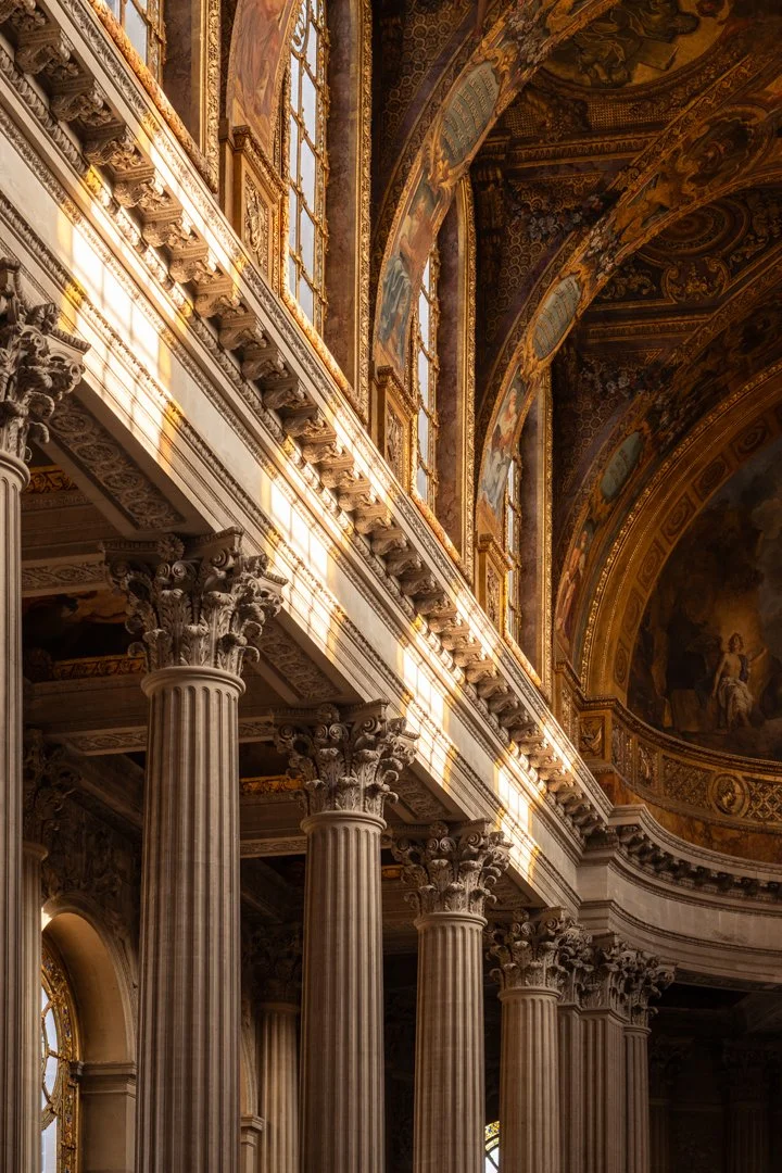 Interior of a grand hall with tall Corinthian columns and ornate decorations, featuring stained glass windows and detailed ceiling murals.