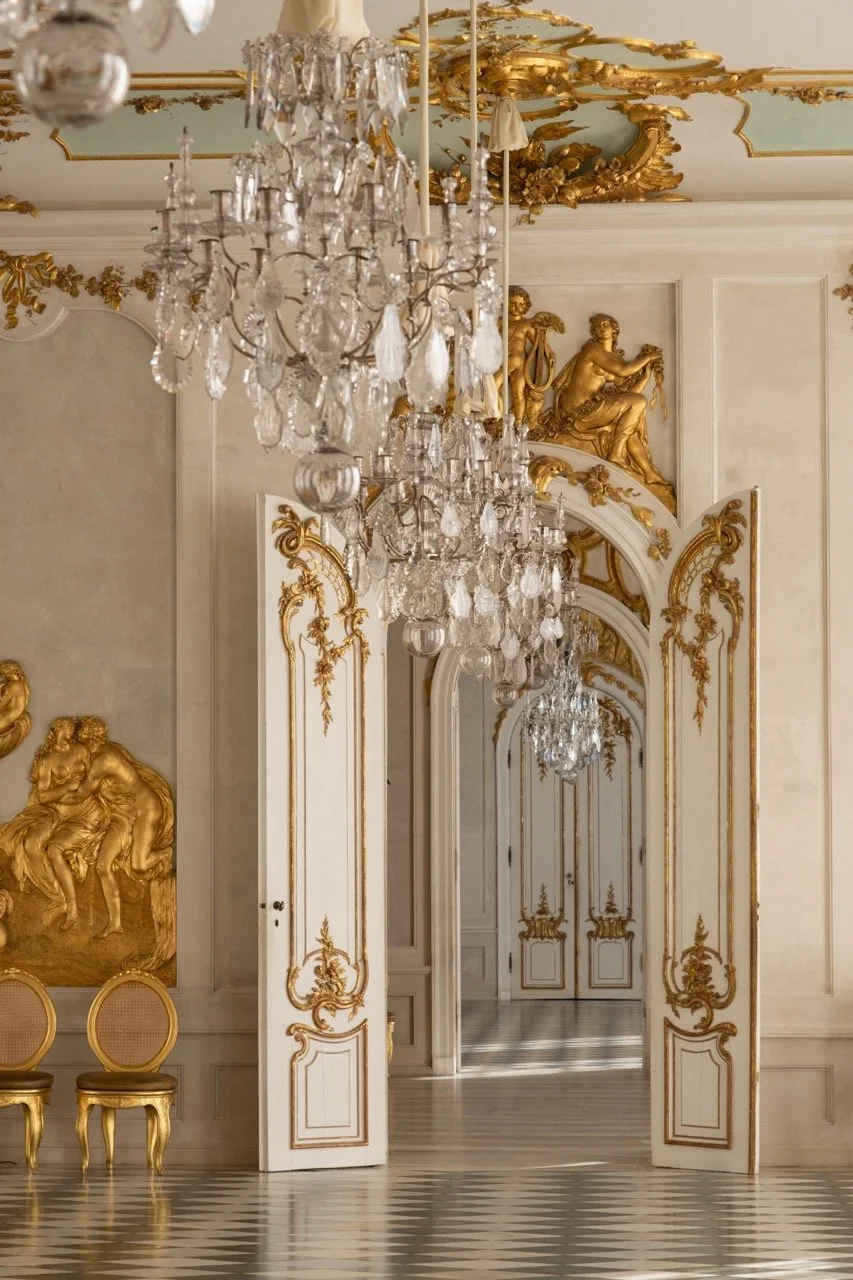 Opulent room with ornate white and gold decor, crystal chandeliers, gold statues, and gilded chairs